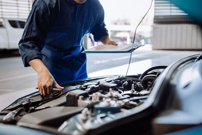 Midsection of mechanic examining car