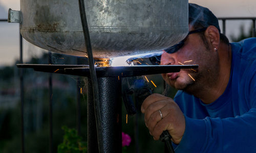 Mid adult man welding metal by railing during sunset