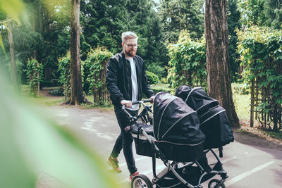 Full length of man pushing baby carriage on footpath