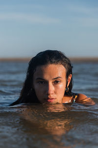 Serene female with wet hair swimming in calm sea in summer evening and looking at camera