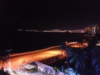 Illuminated cityscape by sea against clear sky at night