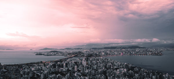 Aerial view of cityscape by sea against cloudy sky during sunset