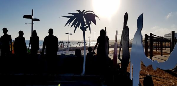 Silhouette people standing by palm trees against sky during sunset