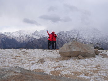 Couple with hand raised standing against snowcapped mountains