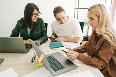 Female colleagues analyze social media marketing at business meeting using mobile phone and laptops.