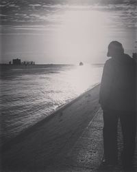 Rear view of man standing on beach against sky