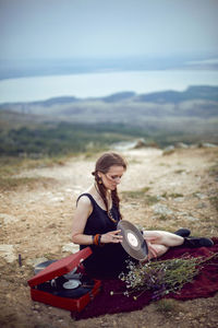 Young woman lies in nature in a black dress next to an old gramophone and listens to music