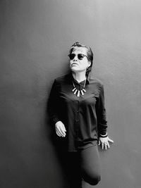 Woman in sunglasses and necklace standing against wall