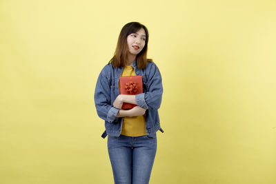 Portrait of smiling young woman standing against yellow background