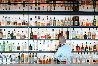 Bartender against arranged bottles in shelf