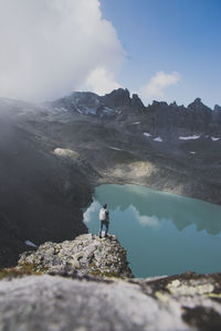 Rear view of man standing on rock looking at view of lake