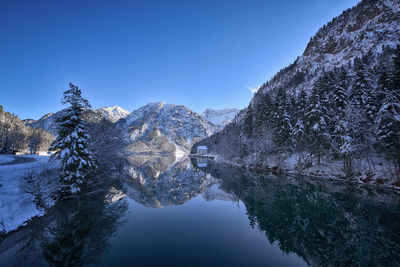 Scenic view of lake by mountains against clear blue sky during winter