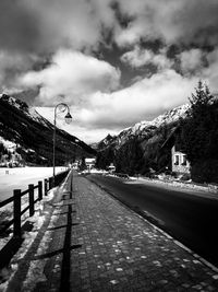 Street by footpath against sky in city