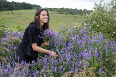 Portrait of woman standing amidst purple flowering plants on field