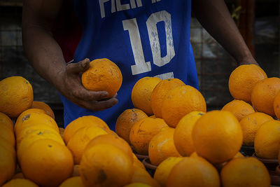 Midsection of vendor holding orange at street market stall