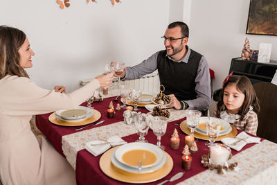 Smiling couple with decorative glasses of alcoholic drink above served table with burning candles on christmas day at home