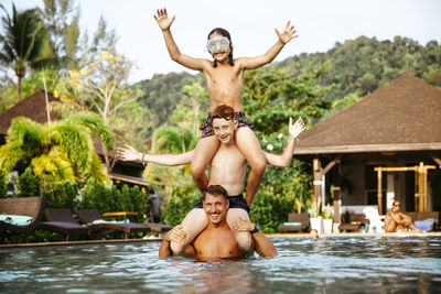 Happy father carrying children on shoulders while enjoying in swimming pool during vacation