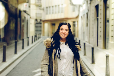 Portrait of smiling young woman standing on footpath in city