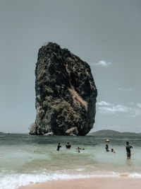People on rocks by sea against sky