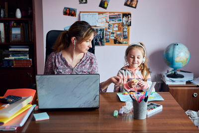 Mother using laptop while sitting at home with daughter