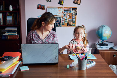 Mother using laptop while sitting at home with daughter