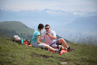 Couple sitting on mountain against sky
