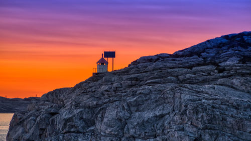 Lighthouse on rock by building against sky during sunset