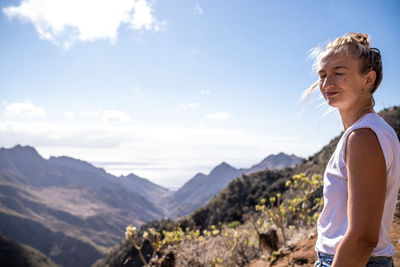 Side view of woman standing on mountain against sky