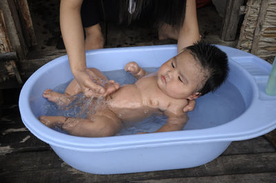 Cropped hands of mother holding baby boy in bathtub