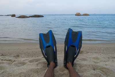 Low section of man wearing diving flippers at trikora beach against sky