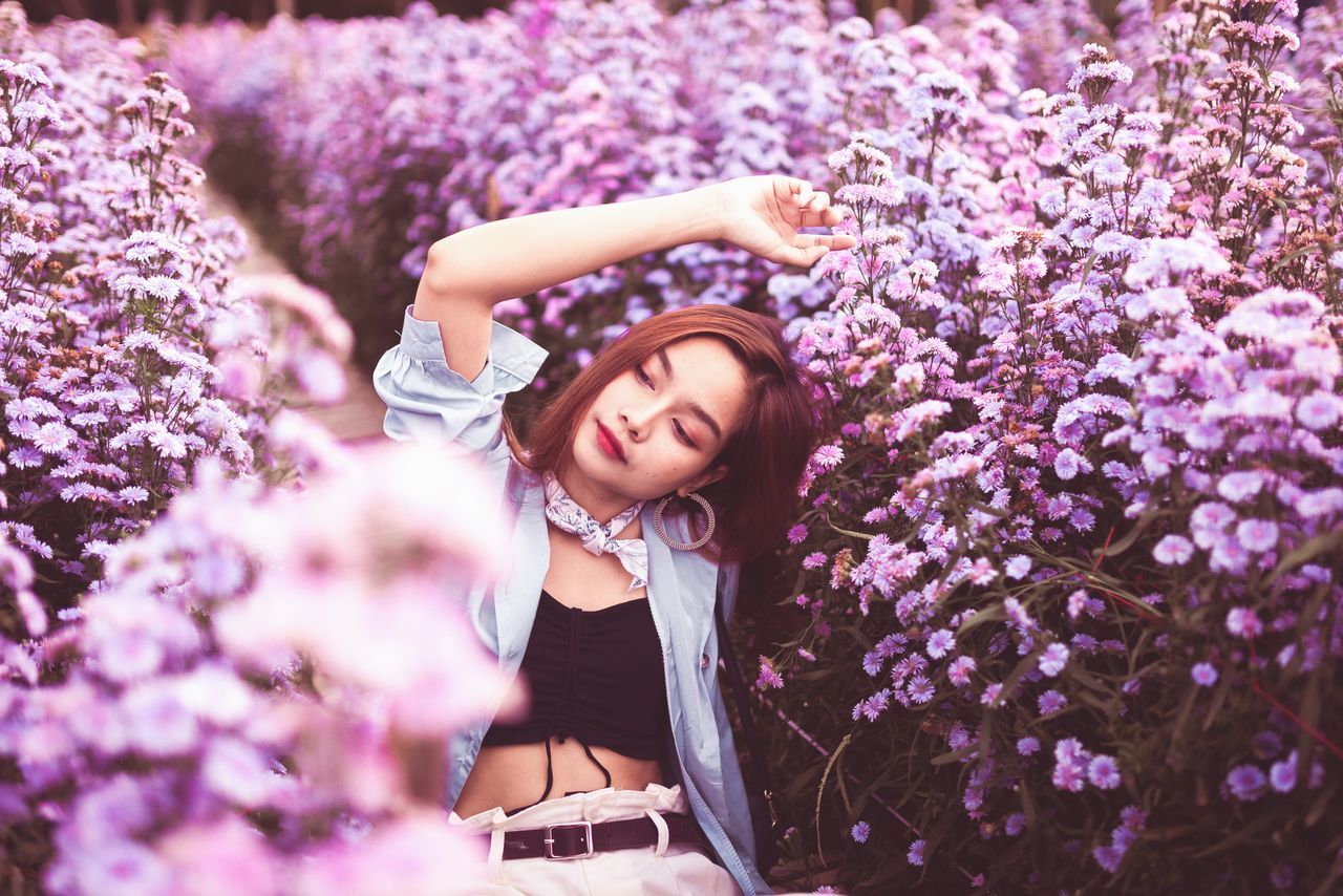 flower, flowering plant, spring, plant, purple, one person, women, beauty in nature, adult, young adult, nature, lilac, blossom, freshness, springtime, pink, happiness, smiling, lavender, lifestyles, relaxation, portrait, outdoors, emotion, cheerful, hairstyle, fragility, female, clothing, leisure activity, growth, selective focus, fashion, summer, cherry blossom, looking, sunlight, tree, technology, day, positive emotion, eyes closed, scented, casual clothing, enjoyment, brown hair, garden, field