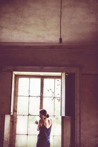 Rear view of woman standing against window in abandoned home