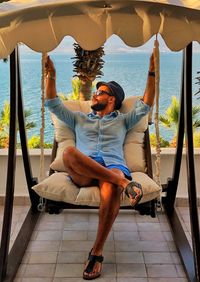 Full length of man relaxing against sea on swing