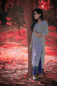 Woman standing by tree trunk during autumn