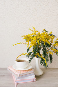 A beautiful composition of mimosa branches and a white tea cup with a saucer and a stack 