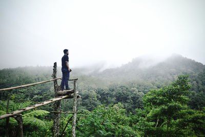 Full length of man standing at observation point against mountain during foggy weather