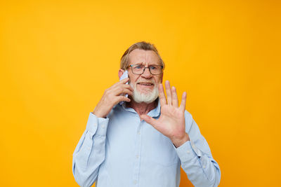 Senior man talking on phone against yellow background