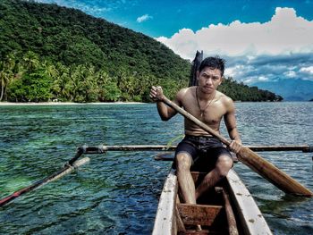 Shirtless man rowing outrigger boat in sea