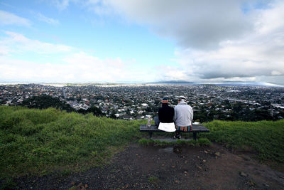 Rear view of couple sitting on landscape against sky