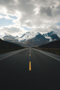 Road leading towards snowcapped mountains against sky