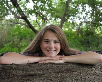 Portrait of smiling young woman against tree trunk