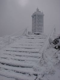 Snow covered land by building against sky