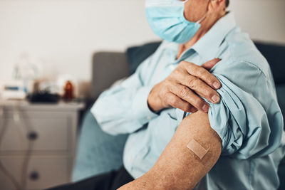 Senior man patient holding shirt sleeve up with a plaster in place of injection of vaccine. covid-19