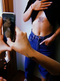 Cropped hands of woman photographing friend tattoo at home