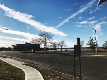 Empty road by bare trees against sky