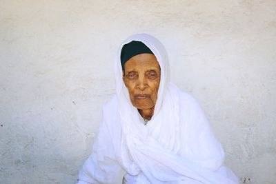 Portrait of senior woman sitting against wall