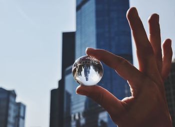 Close-up of hand holding crystal ball against skyline