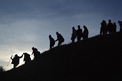 Low angle view of silhouette friends on hill against sky