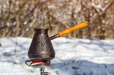 Copper turk with a wooden handle for making coffee on a background of snow in woods