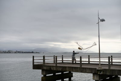 Man on pier by sea against sky